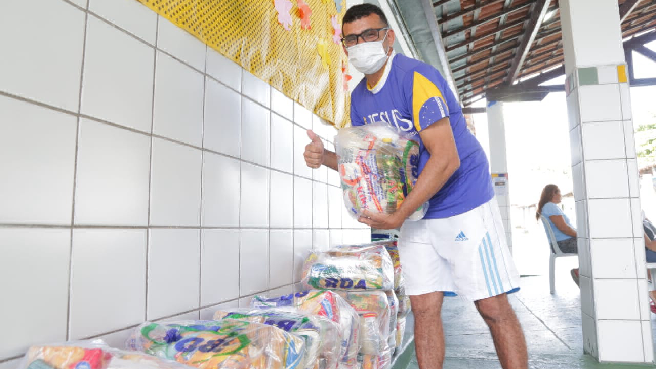 homem com máscara hospitalar segurando cesta básica fazendo legal com a mão para a foto